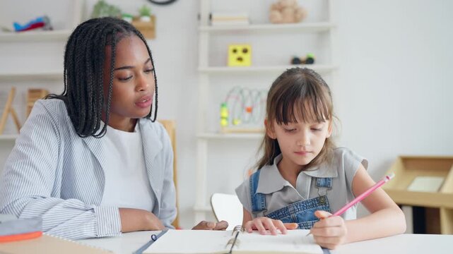 African woman tutor guide young child through art and painting in nursery. 
