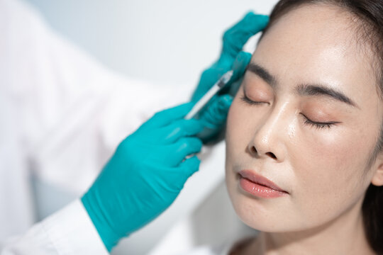 Close-up of a woman receiving a cosmetic injection on her forehead from a gloved medical professional with eyes closed