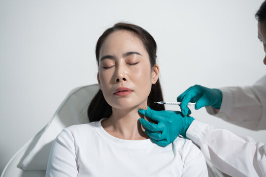 Woman getting a cosmetic neck injection from a gloved doctor in a bright clinic.
