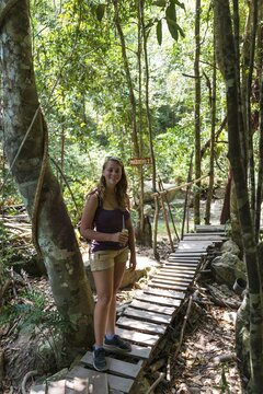 Tourist smiling, holding a drink, standing on a boardwalk in the woods, path to the Na Muang waterfalls, Ko Samui, Thailand