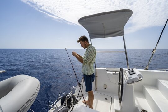 Young man fishing on a boat, sailing catamaran, sailing trip, Dodecanese, Greece