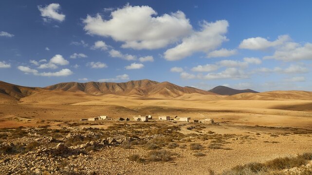 Island interior, barren landscape, reddish brown hills, ruins of buildings further away, sparse vegetation, blue sky, white clouds, Fuerteventura, Canary Islands, Spain