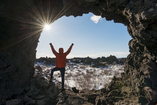Man stretches arms in the air, rock arch with sunbeams, volcanic landscape, volcanic area Krafla, Dimmuborgir National Park, M&yacute;vatn, Iceland