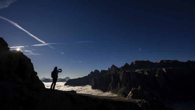 Mobile phone photographer on ridge with Dolomites mountains in the background, Corvara, Dolomites, Italy