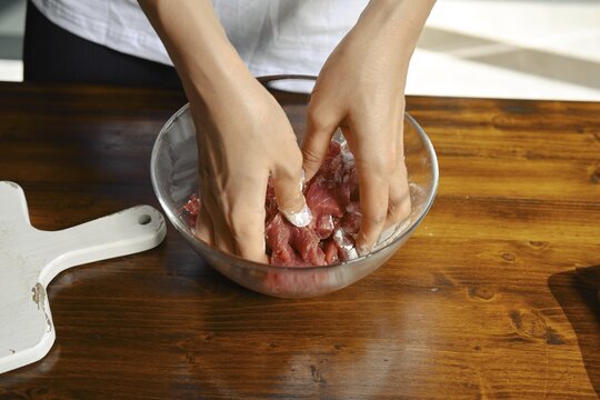Close-up view of female hands mixing lean meat and starch in a transparent bowl, emphasizing the preparation of a healthy dish