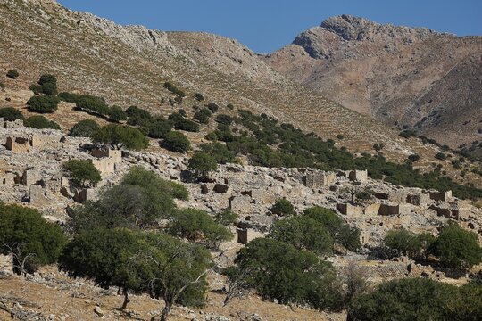 Stone ruins in front of a rocky mountain landscape with scattered trees and blue sky, Lost Place, Abandoned Village, Mikro Chorio, Church of the Assumption of Mary, Zero Waste Island, Tilos, Dodecanese, Greek Islands, Greece