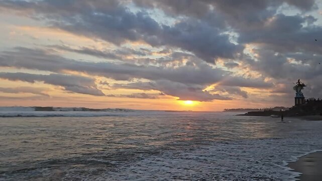 Wide panning shot of beautiful sunset over Pererenan Beach in Bali with surfers riding ocean waves. Scenic tropical sea coast stock footage.