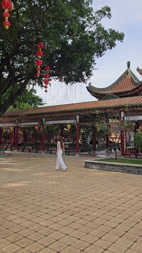 Cinematic vertical view of a female tourist exploring ancient Chinese architecture and covered walkways at Baomo Garden river park. Travel stock.