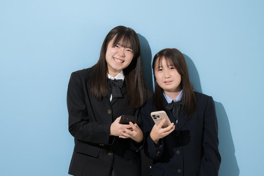 スマートフォン(スマホ)を見る日本人女子中学生、女子高校生　2人で情報を共有する学校生活とコミュニケーション、スマホの安全な使い方イメージ　カメラ目線