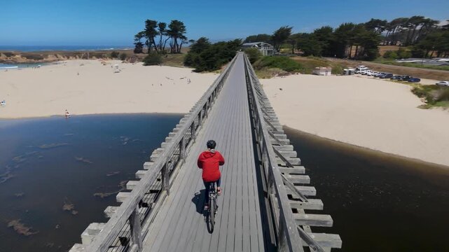 A mature woman rides a bike over the Pudding Creek trestle bridge in Fort Bragg California enjoying a sunny day by the beach