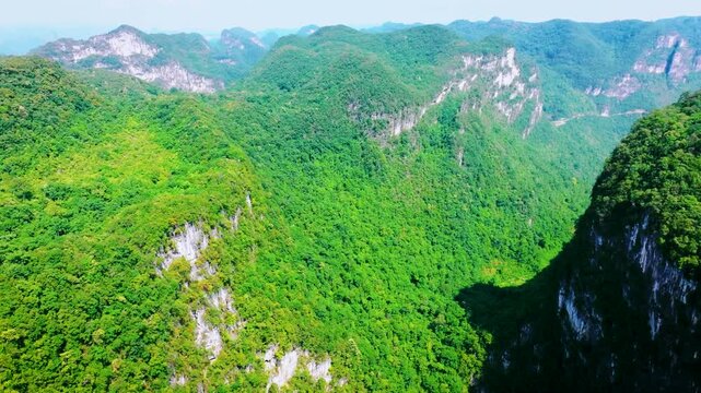 Aerial view of a massive karst sinkhole surrounded by steep green cliffs and dense forest in summer