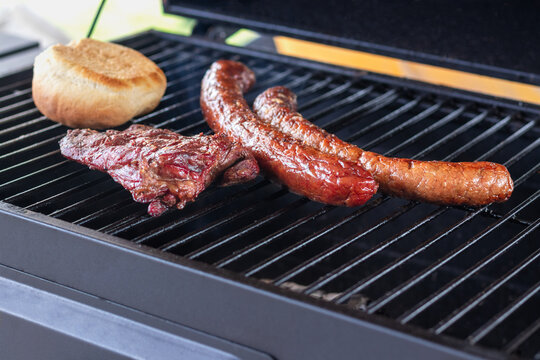 Close up of grilled meat, sausages, and buns warming up on a black BBQ grill