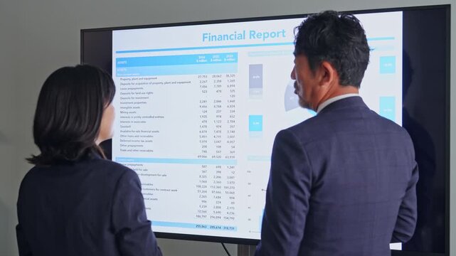画面を見ながら会話するビジネスパーソンのグループ。会議、チームワーク、同僚、人材、相談、研修、指導