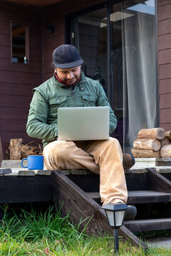 Hispanic focused man using a portable computer outdoors on a rustic cottage deck, vertical view