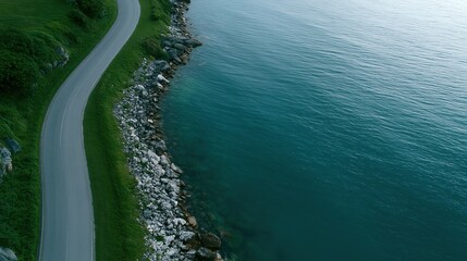 Fototapeta premium Scenic coastal road winding alongside a vast, tranquil turquoise ocean with rocky shores and green hills