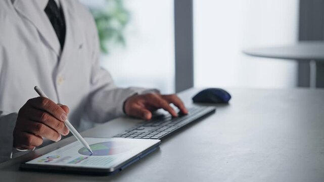 A man in a white coat working with a laptop and a tablet PC. Science, research, medical, doctor, experiment, data, analysis.