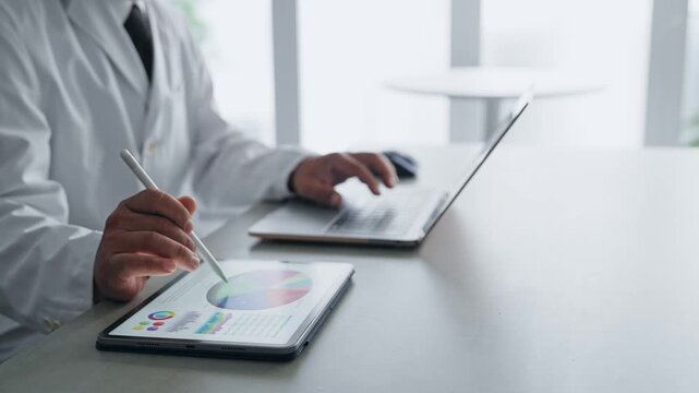 A man in a white coat working with a laptop and a tablet PC. Science, research, medical, doctor, experiment, data, analysis.