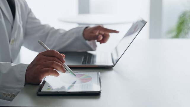 A man in a white coat working with a laptop and a tablet PC. Science, research, medical, doctor, experiment, data, analysis.