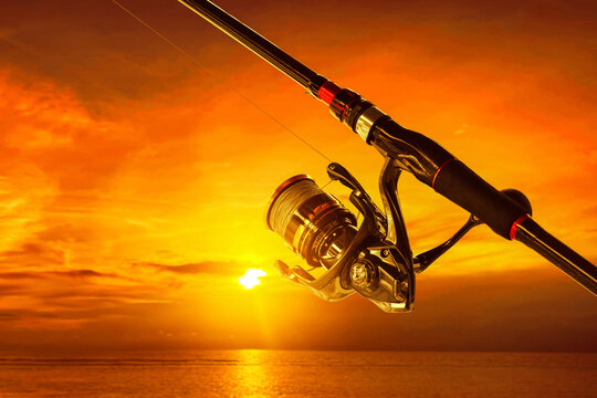 Closeup of fishing rod and spinning reel at ocean with sunset sky