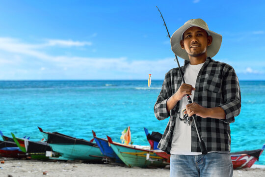 Portrait of man smiling with fishing rod and boats on beach under blue sky
