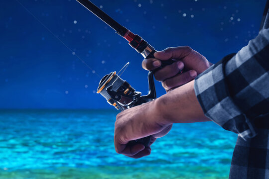 Closeup of hand holding fishing rod over ocean at night