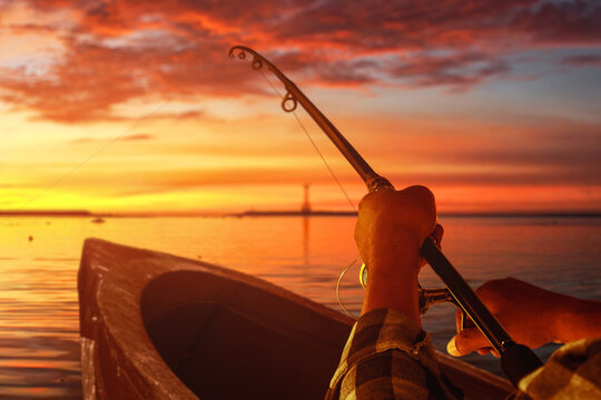 Man fishing from wooden boat on calm lake at sunset