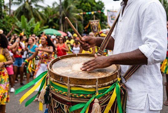 Musician playing a traditional Brazilian drum with colorful ribbons at a street festival parade