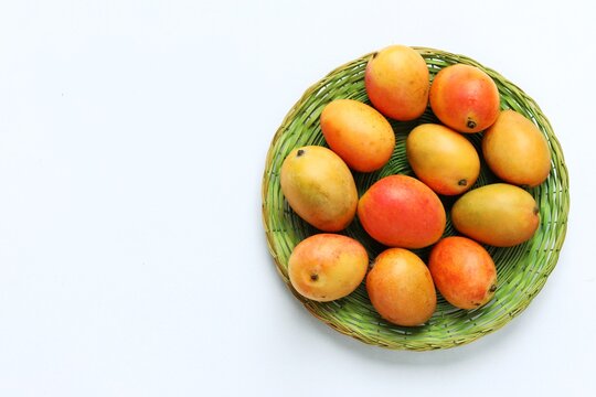 Top view of ripe yellow alphonso mango fruits in a green woven plate isolated on a white background