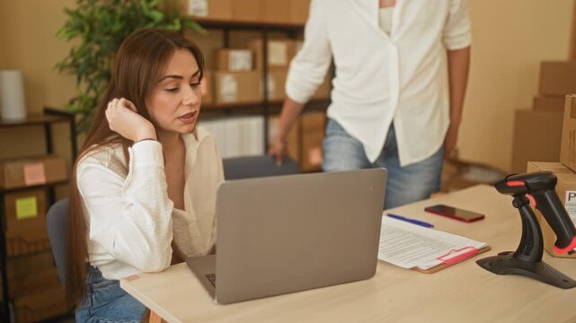 Woman points to laptop screen while seated beside colleague in building office; collaboration planning.