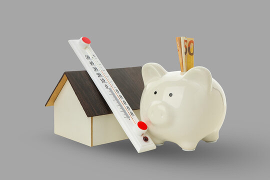 A piggy bank filled with cash and a thermometer near a house