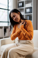 Obraz premium Woman experiencing sudden severe chest pain at home, grabbing her chest with hands, suffering from angina symptoms, heart attack, or anxiety, seeking relief