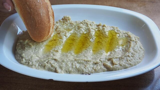 Dipping bread in a bowl of hummus and olive oil