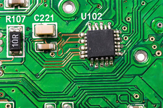 A close-up shot of a green printed circuit board with surface-mount electronic components including an integrated circuit, resistor, and capacitors.