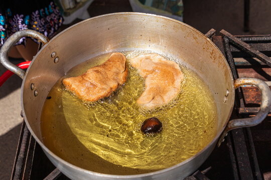 A close-up shot of a large, golden-brown Empanada de Viento (wind empanada), a traditional Ecuadorian fried cheese pastry, frying in hot oil in old pot