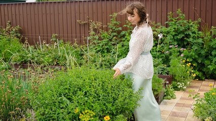 Woman standing among vegetable beds and spearmint plants in garden - Concept of Mentha spicata   © Maria A