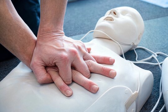 Performing CPR chest compressions on a medical training mannequin in a classroom
