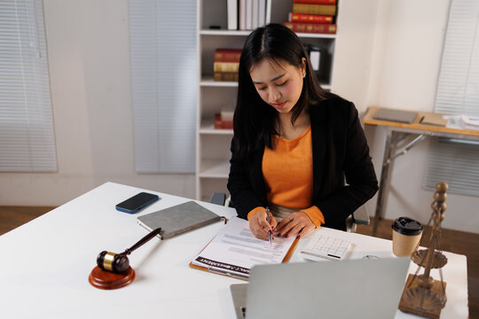 Young asian woman lawyer analyzing legal documents, signing a contract, and managing paperwork in a law office, representing professionalism, justice, and corporate law
