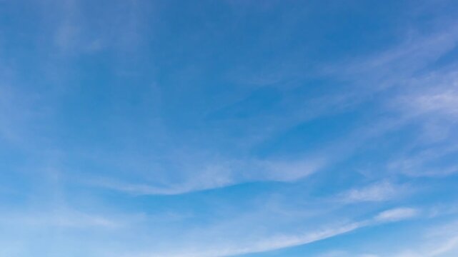Peaceful daytime sky time-lapse with soft white clouds flowing in a deep blue atmosphere.