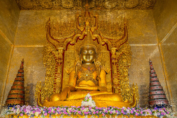 Fototapeta premium Magnificent golden Buddha statue inside the beautifully decorated pavilion at Wat Thai Wattanaram temple in Mae Sot, Tak, Thailand. A stunning example of sacred Mon Burmese art.
