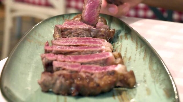 Sliced grilled beef steak on a platter being picked up with a fork in a restaurant