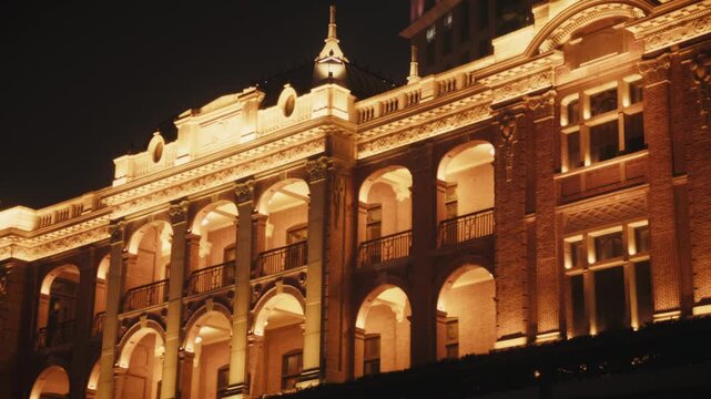 Night shot of a colonial-era heritage building facade on The Bund, Shanghai. Two levels of grand arched colonnades with wrought iron balcony railings, terracotta brick and ornate carved stone cornice.