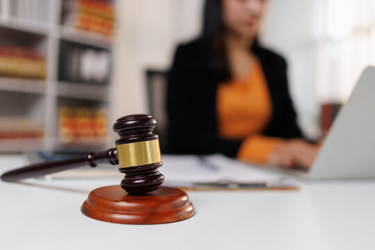 Gavel resting on a white desk. Signifying legal authority and justice. With a female professional lawyer working diligently on a laptop in the background