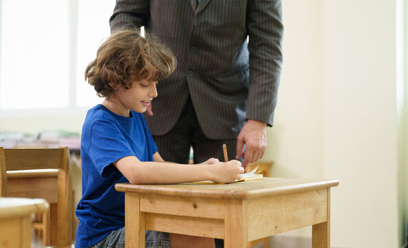 Teacher supports a young student during a classroom writing activity, encouraging confidence, concentration, and positive learning through individual guidance.