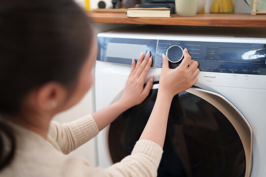 Asian Woman adjusting washing machine settings before starting a laundry cycle, highlighting smart home appliances, convenience, and fabric care.