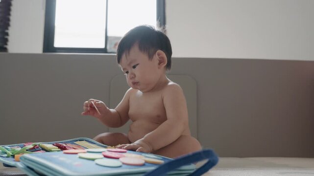 Cute Asian baby boy playing with busy board toy at home, early childhood development.