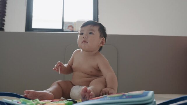 Cute Asian baby boy playing with busy board toy at home, early childhood development.