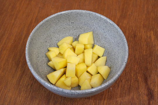 Fresh raw diced yellow potato cubes in grey ceramic bowl on wooden table