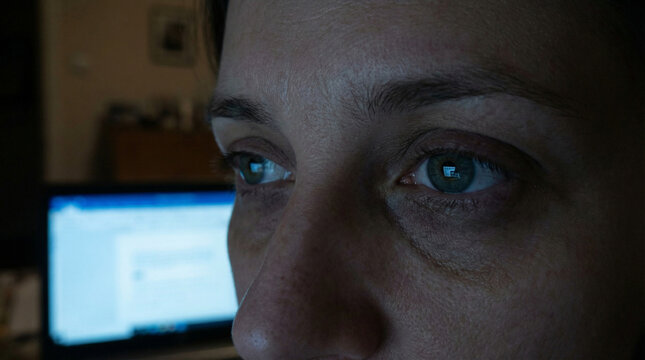 Intense focus in the glow of a laptop screen, revealing the subtle strain and dedication of late-night work, with eyes reflecting the blue light of technology