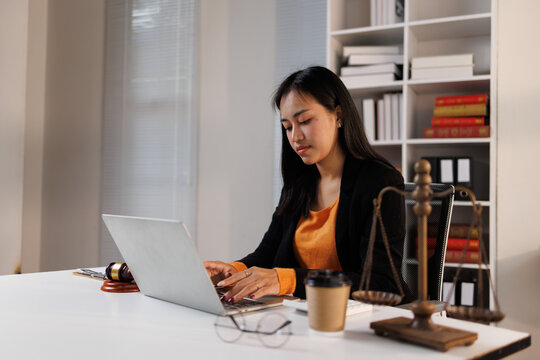 Young asian woman working on a laptop in a contemporary office setting, representing legal work, justice, and the integration of technology in the modern legal field