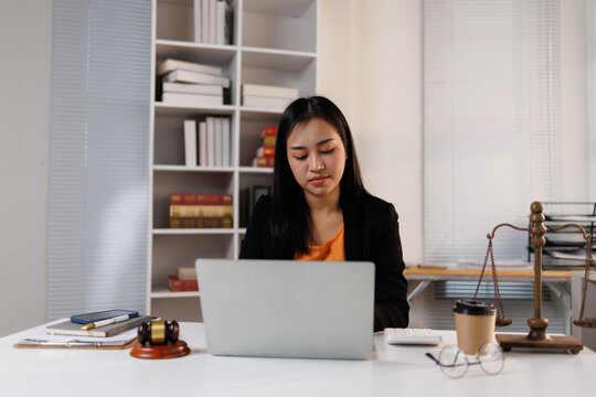 Female lawyer working on laptop, researching cases and legal documents in a law office or firm, representing justice and legal assistance concepts